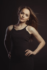 Naklejka premium Beautiful brunette model in black dress with fluttering hair with wind