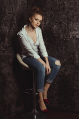 Fototapeta premium Attractive young model sitting on a chair in striped and torn jeans
