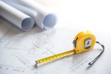 architectural drawing plan of house project, blueprint rolls and yellow tape measure (measuring tape) on work table, building construction industry concepts