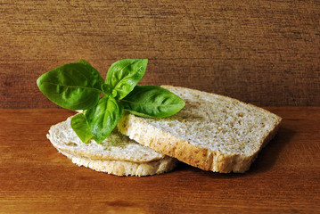 Two slices of toast, made from whole meal, on a wooden plate and a leaf of Basil