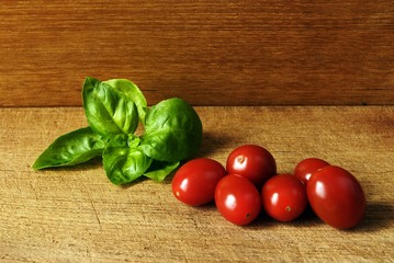 Grape tomatoes and a leafe of basil on a wooden plate