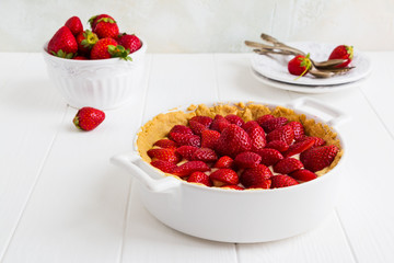 Homemade French tart with strawberries in a custard. White pan, fresh berries and vintage plates on the wooden table.