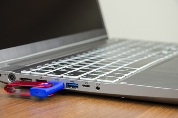 Close-up view of a silver laptop with attached blue flash disk on a wooden table and on a white background