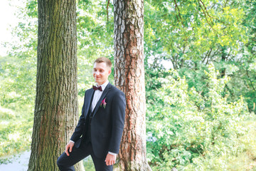 Elegant groom in black costume and purple bow-tie. Groom on his wedding day.Gorgeous smiling groom.