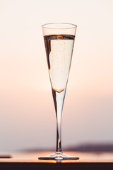 Glass of prosecco at a wooden pier at sunset. Luxury resort vacation concept. Festive relax getaway background.