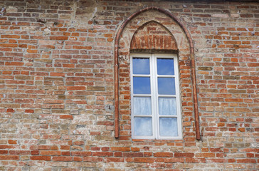 Fototapeta na wymiar Castle window in a medieval style. Double arched window on a facade of medieval wall. Biforium - ancient window with column, old architecture element of Roman and Gothic styles.