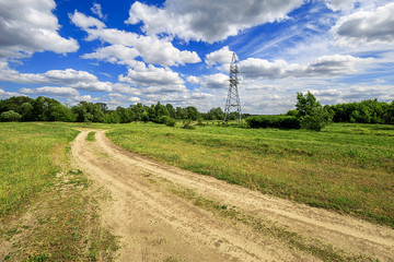Fototapeta premium road and green field with trees and blue sky with clouds sunny day, beautiful rural landscape. Electricity tower standard overhead power line transmission tower