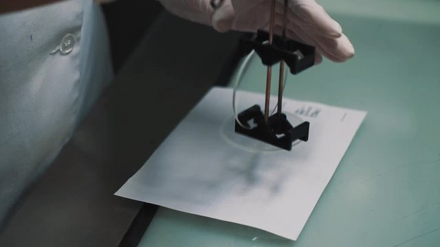 Laboratory worker in white rubber gloves puts lenses on special holder upon paper sheet on table desk, close up