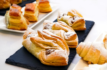 Obraz na płótnie Canvas Ruddy pastry, buns sprinkled with powdered sugar lie on long plates of black color. White tablecloth