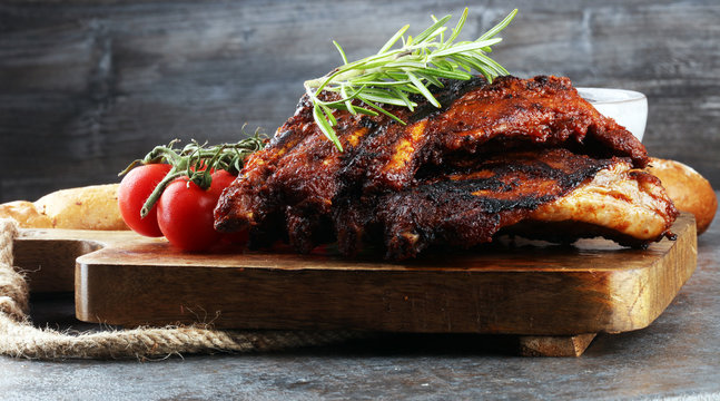 Spicy hot grilled spare ribs from a summer BBQ served with fresh tomatoes on an old vintage wooden cutting board