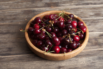 Fresh cherry in a wooden plate on an old wooden background. New harvest. Gardening. Ingredient for cooking and vegetarian food. 