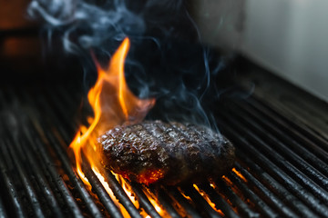 Burger cooking on grill with flames