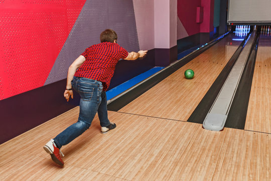 close up of young man in checkered shirt throwing ball to alley in bowling club, leisure and sport concept
