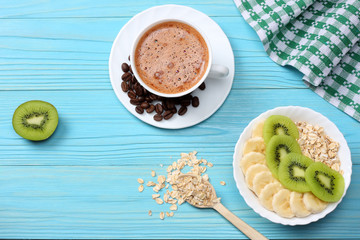 Breakfast with oatmeal porridge, coffee cup and fruits on blue wooden background. Oatmeal with kiwi and banana. Healthy breakfast concept. Top view