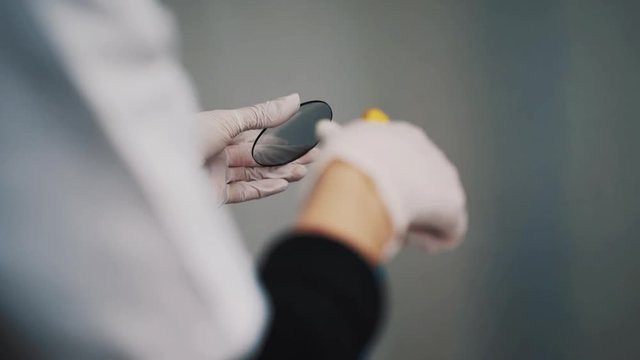 Engineer in white robe and rubber gloves using air compressor on wet glass lens at laboratory, close up