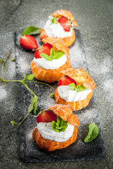 Summer desserts. Homemade baking. Cake profiteroles with whipped cream, fresh strawberries, mint and sprinkling of powdered sugar. On a black stone table. Copy space