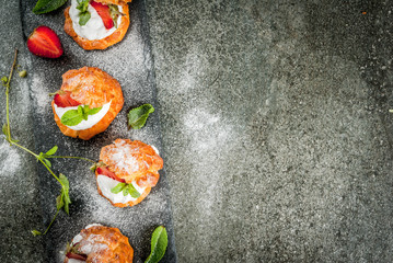 Summer desserts. Homemade baking. Cake profiteroles with whipped cream, fresh strawberries, mint and sprinkling of powdered sugar. On a black stone table. Copy space top view
