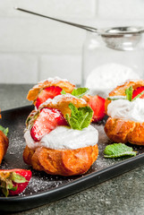 Summer desserts. Homemade baking. Cake profiteroles with whipped cream, fresh strawberries, mint and sprinkling of powdered sugar. On a black stone table. Copy space