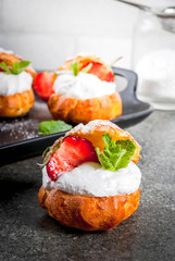 Summer desserts. Homemade baking. Cake profiteroles with whipped cream, fresh strawberries, mint and sprinkling of powdered sugar. On a black stone table. Copy space