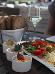 Wooden party table served with glass of white wine and horseradish, dips, pickles, tomatoes, prosciutto, scratchings and bread.