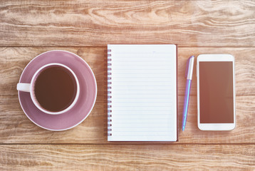 Top view of note pad, wood table with coffee, pen and smart phone retro styled.