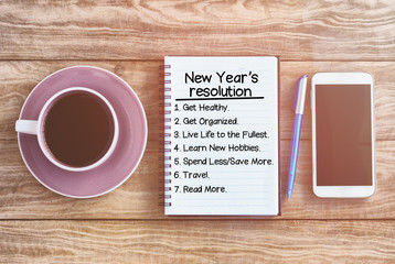 New year's resolution list on note pad, wood table with coffee, pen and smart phone retro styled.
