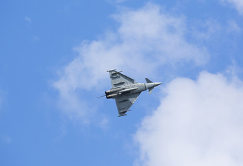 Modern jet fighter flying high against the blue sky with some clouds.
