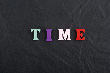 Time word on black board background composed from colorful abc alphabet block wooden letters, copy space for ad text. Learning english concept.