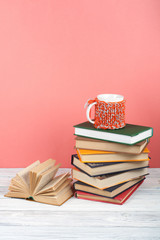 Book stacking. Open book, hardback books on wooden table and pink background. Back to school. Copy space for text.