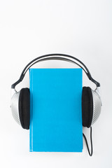 Audiobook on white background. Headphones put over blue hardback book, empty cover, copy space for ad text. Distance education, e-learning concept.