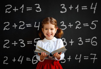 Happy schoolgirl preschool girl with book near school blackboard