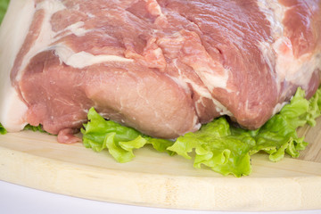 Raw cervical carbonate of pork on cutting board with leaves of green salad, isolated on white background