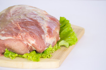 Raw cervical carbonate of pork on cutting board with leaves of green salad, isolated on white background