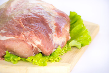 Raw cervical carbonate of pork on cutting board with leaves of green salad, isolated on white background