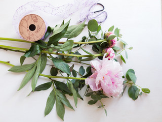 Peonies and eucalyptus with sequin ribbon and scissors on white canvas