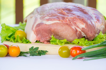 Raw cervical carbonate of pork on cutting board with leaves of green salad, vegetables, tomatoes, parsley and onion, isolated on white background