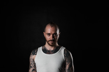 Brutal and brave man in white t-shirt look to the camera. Tattooed strong body person on black background. Tattoo model with short hair style.