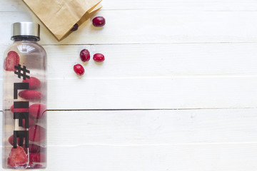 Bottle with refreshing drink, water with strawberry slices, with hashtag #life and package with frozen berries on white wooden background