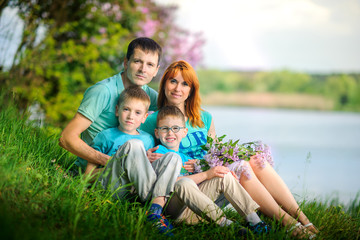 Naklejka na ściany i meble happy family on walk in the park, sit on the river bank with a bouquet of flowers in hands