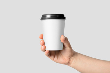 Mockup of male hand holding a Coffee paper cup isolated on light grey background. 