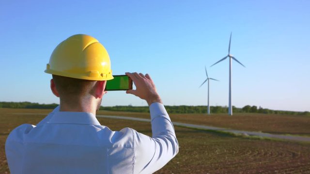 The engineer stands on the background of windmills and takes pictures