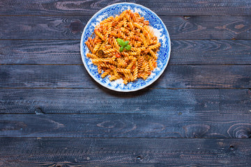 Fusilli pasta with tomato sauce, tomatoes, onion, garlic, dried paprika, olives, pepper and olive oil, on a wooden background.