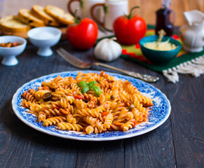 Fusilli pasta with tomato sauce, tomatoes, onion, garlic, dried paprika, olives, pepper and olive oil, on a wooden background.