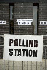 British election polling station sign hanging on  fence in front of black brick wall in London, UK