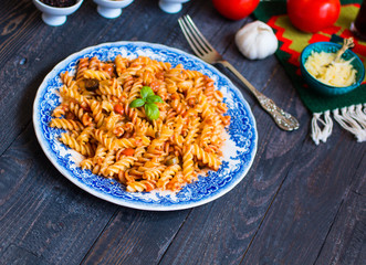 Fusilli pasta with tomato sauce, tomatoes, onion, garlic, dried paprika, olives, pepper and olive oil, on a wooden background.