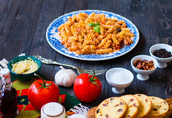 Fusilli pasta with tomato sauce, tomatoes, onion, garlic, dried paprika, olives, pepper and olive oil, on a wooden background.