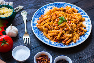 Fusilli pasta with tomato sauce, tomatoes, onion, garlic, dried paprika, olives, pepper and olive oil, on a wooden background.