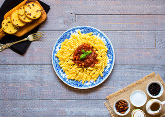 Fusilli pasta with tomato sauce, tomatoes, onion, garlic, dried paprika, olives, pepper and olive oil, on a wooden background.