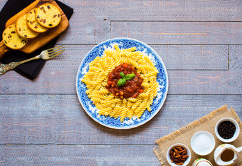 Fusilli pasta with tomato sauce, tomatoes, onion, garlic, dried paprika, olives, pepper and olive oil, on a wooden background.