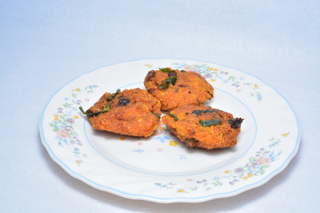 a popular Southern Indian deep fried snack, 'Masala Vadai' with curry leafs the traditional Indian vegetable food on plate isolated with white background